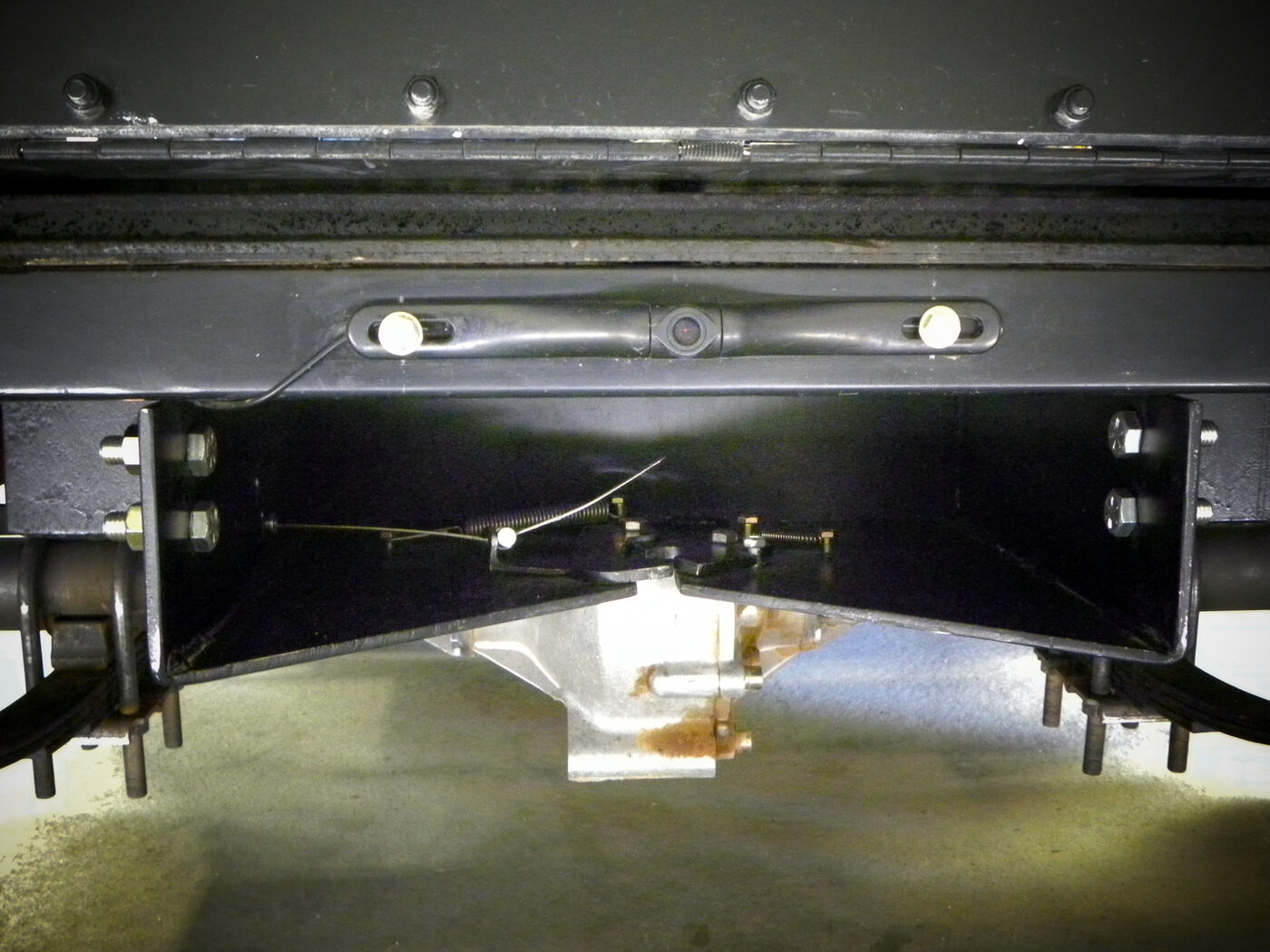 Underside view of the Enabler's rear catch bracket, showing the spring-loaded hook mechanism and the backup camera mounted in the crossbar above it