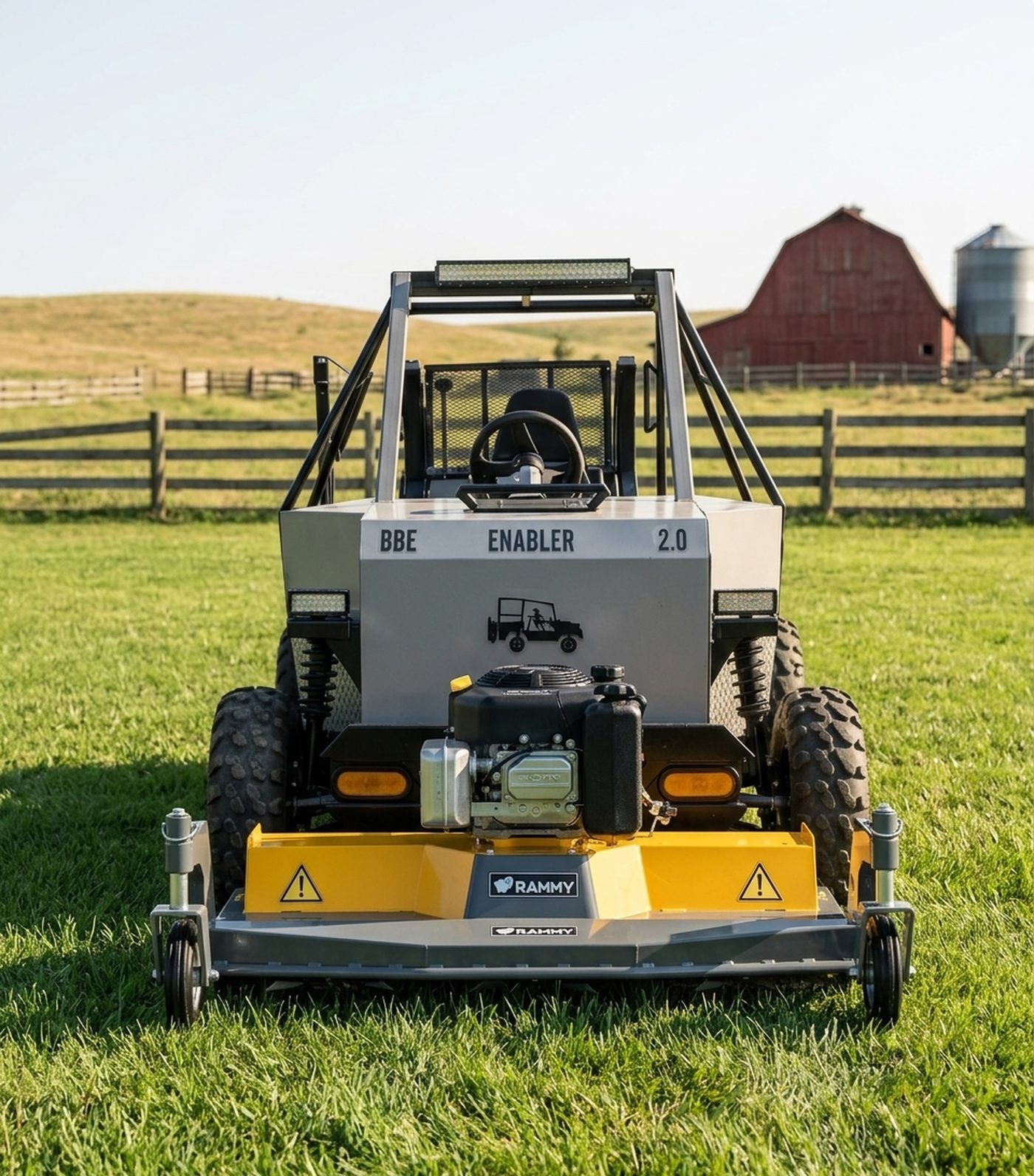 Front view of the Enabler 2.0 with a Rammy mower attachment mounted on front, parked in a pasture with a barn and grain silo in the background
