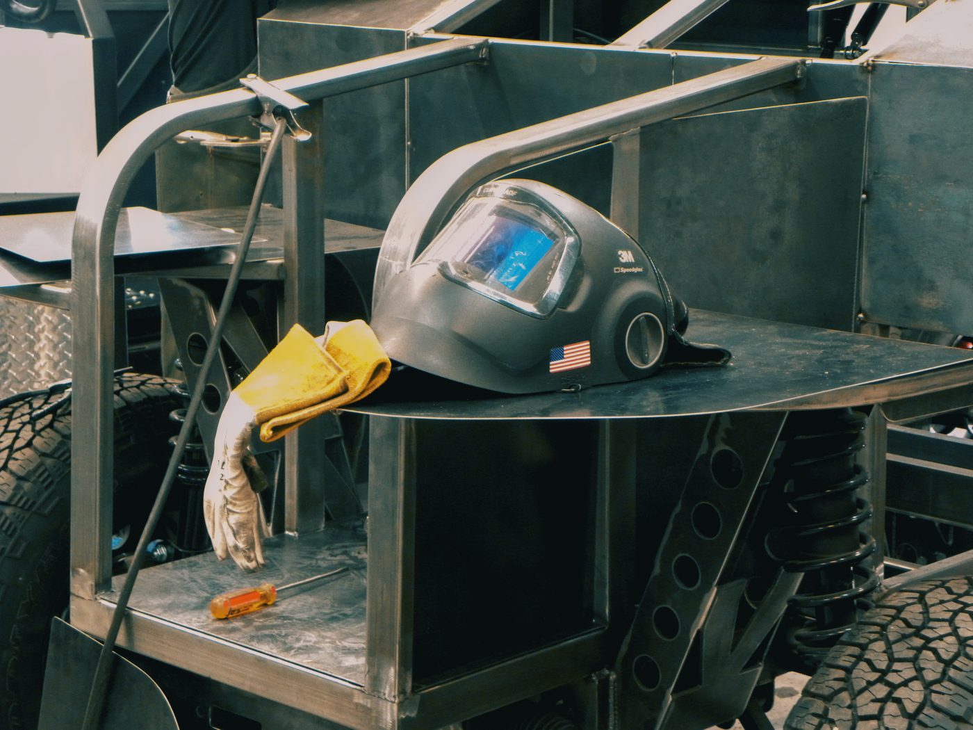 Welding helmet and gloves resting on the bare steel chassis between welds