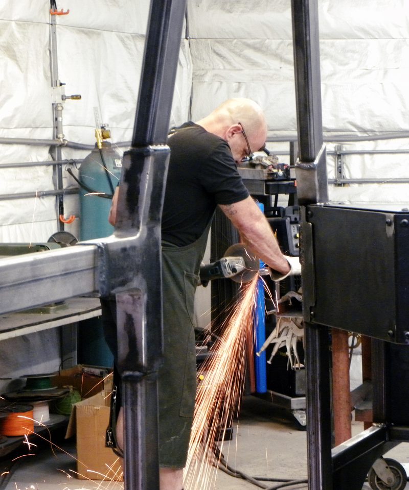 Fabricator grinding a weld on the vehicle frame at the bench