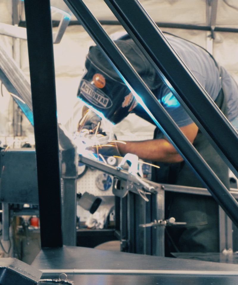 Fabricator welding inside the Enabler's frame, arc light and sparks visible