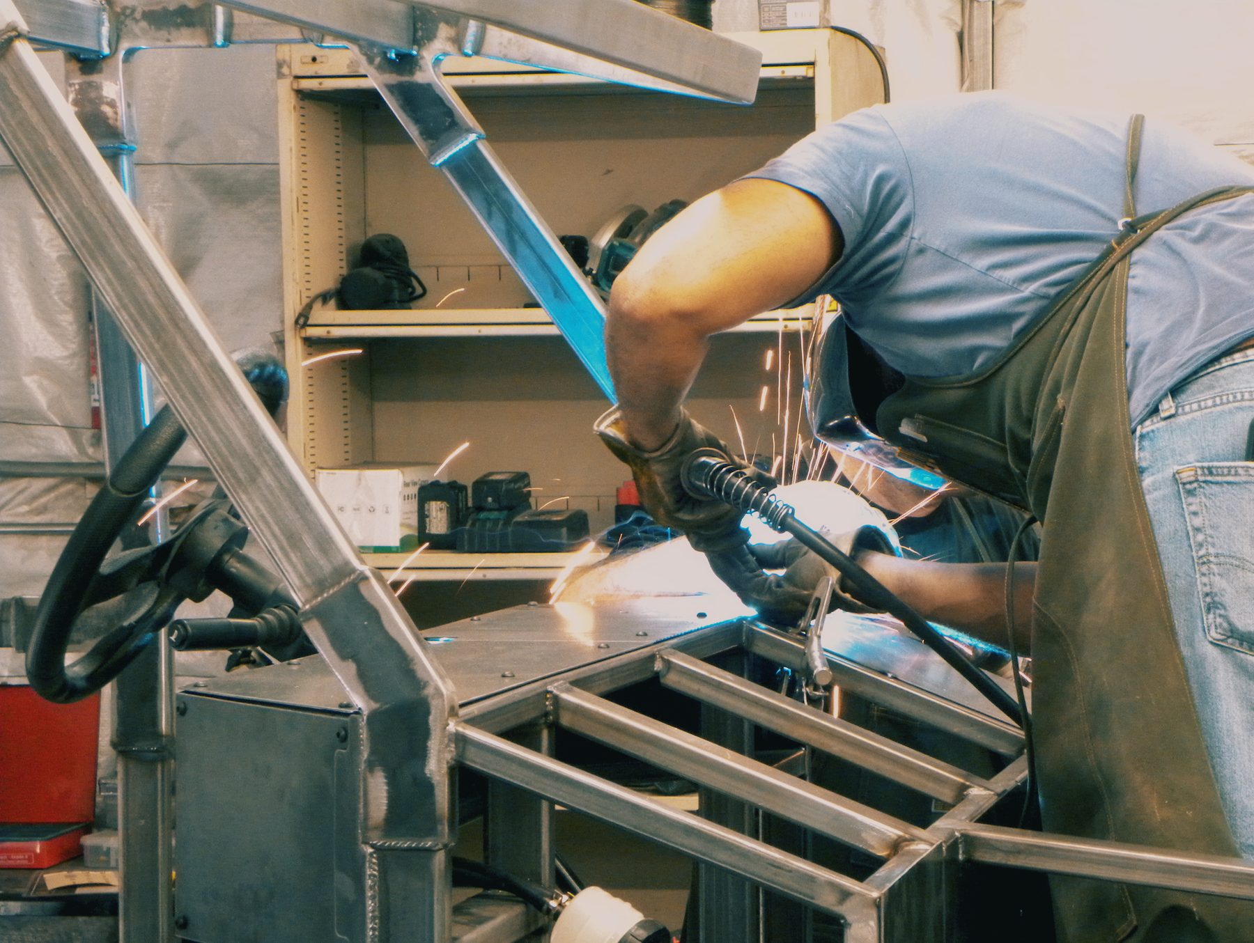 A fabricator welding the Enabler chassis, arc light and sparks visible across the bare steel frame